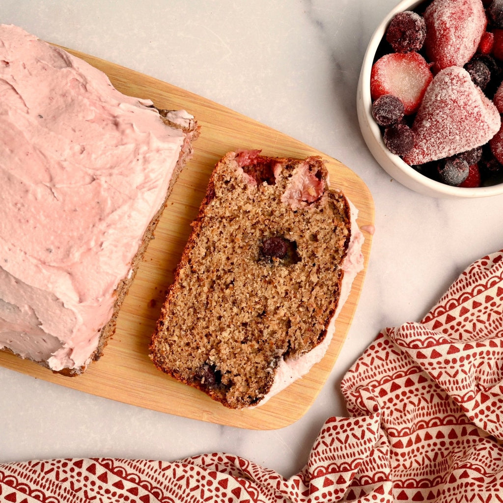 A wooden cutting board with a loaf of homemade cashew berry banana bread sliced