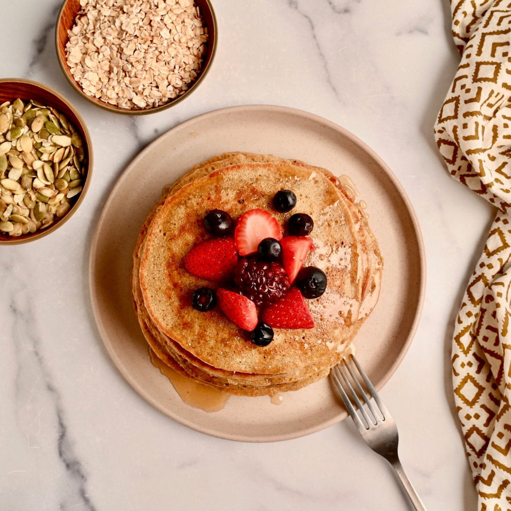 A plate with a stack of pancakes and fresh fruit on top