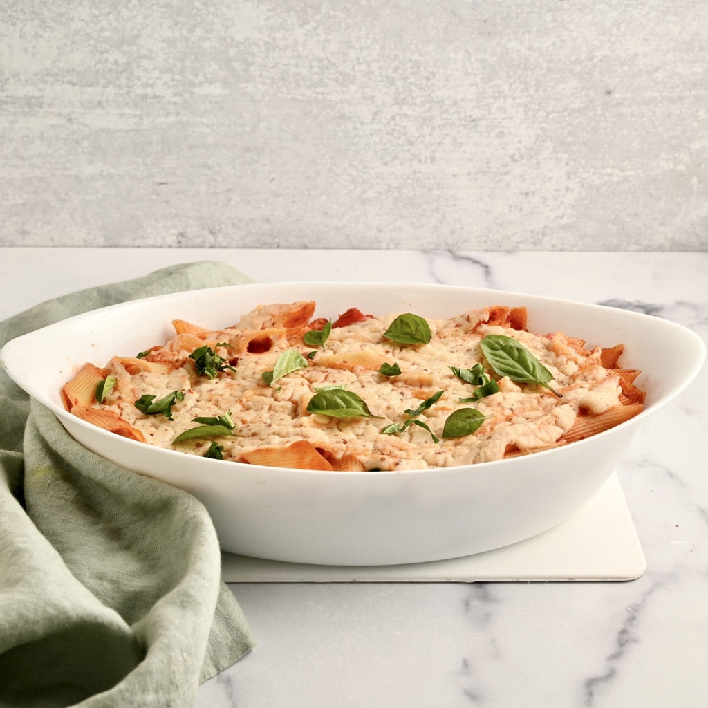 A big white ceramic bowl filled with noodles red tomato sauce and melted white cheese  on top with some fresh sprigs of green herbs for garnish