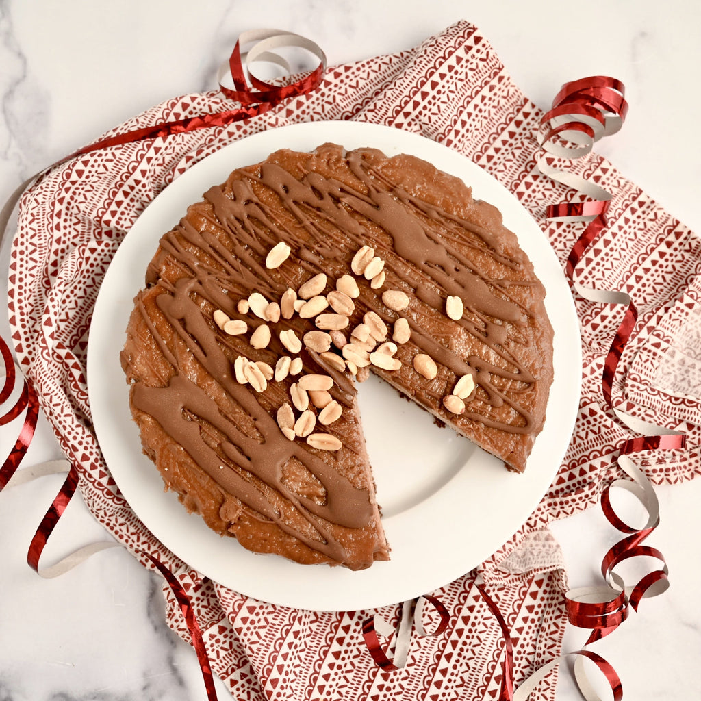 White and red table cloth laying across a white and gray marble countertop with a white plate on top of the towel on the white plate is a peanut butter pie topped with roasted peanuts a red and white ribbon surrounds the white plate