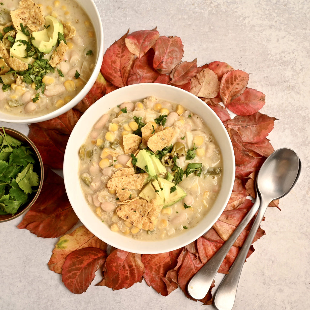 A pile of leaves with a white ceramic bowl in the middle filled with white bean chili 