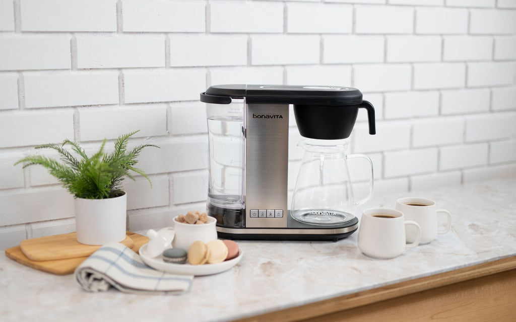 The Enthusiast Coffee Brewer sits on a white marble countertop in a modern minimalist kitchen.